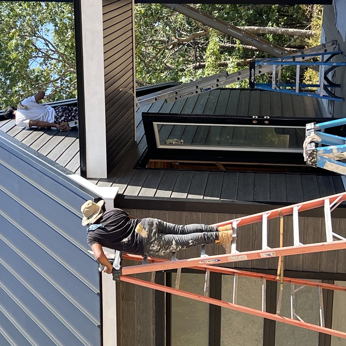 Suffolk County home mid-exterior-repaint — ladders up against a two-story colonial, one elevation finished in fresh color, equipment staged neatly on the lawn.